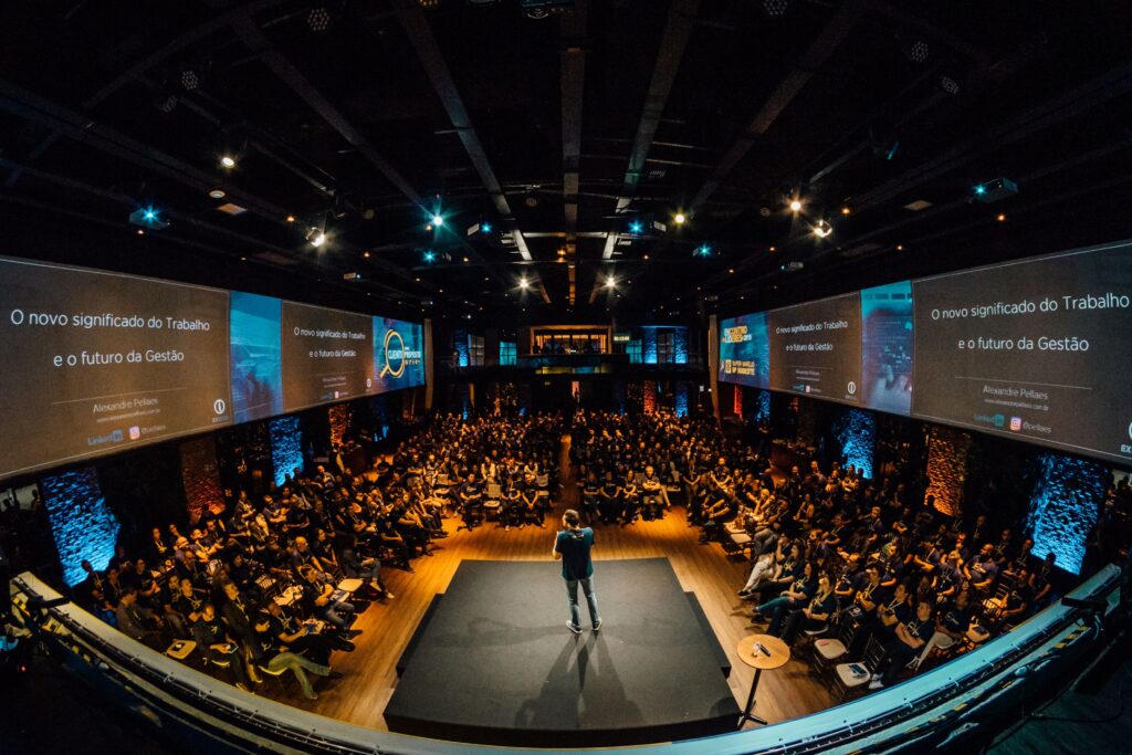 People attending a conference call with a man on stage speaking towards them