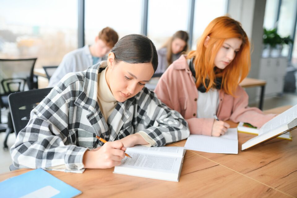 students sit at shared desk making notes studying for an exam