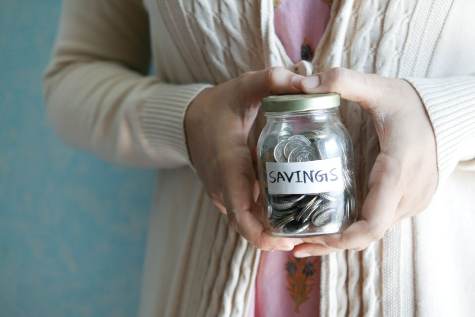 A woman holding a jar of coins with the word savings on it