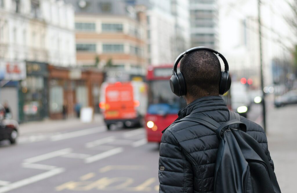 A man wearing headphones waiting for the bus. 