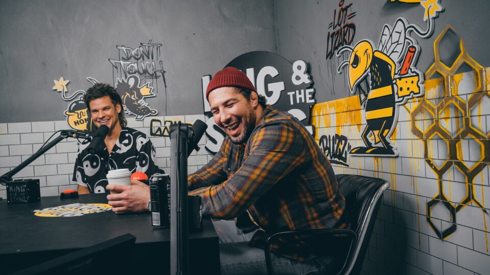 Two men laughing into their mics and talking on a podcast