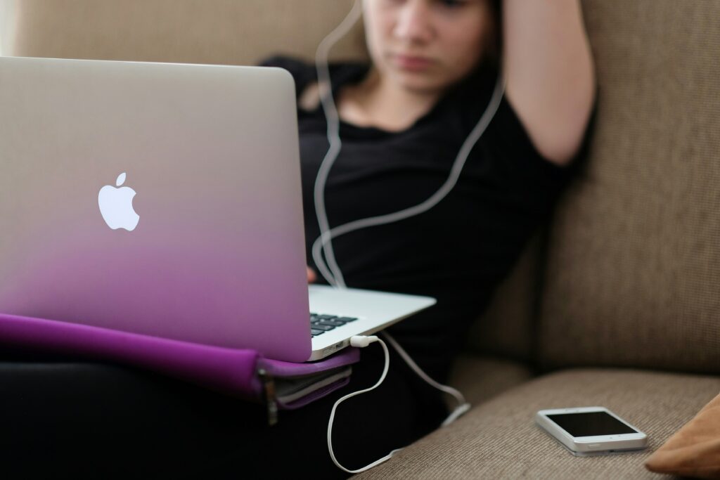 A girl laying down with her headphones in and her laptop open