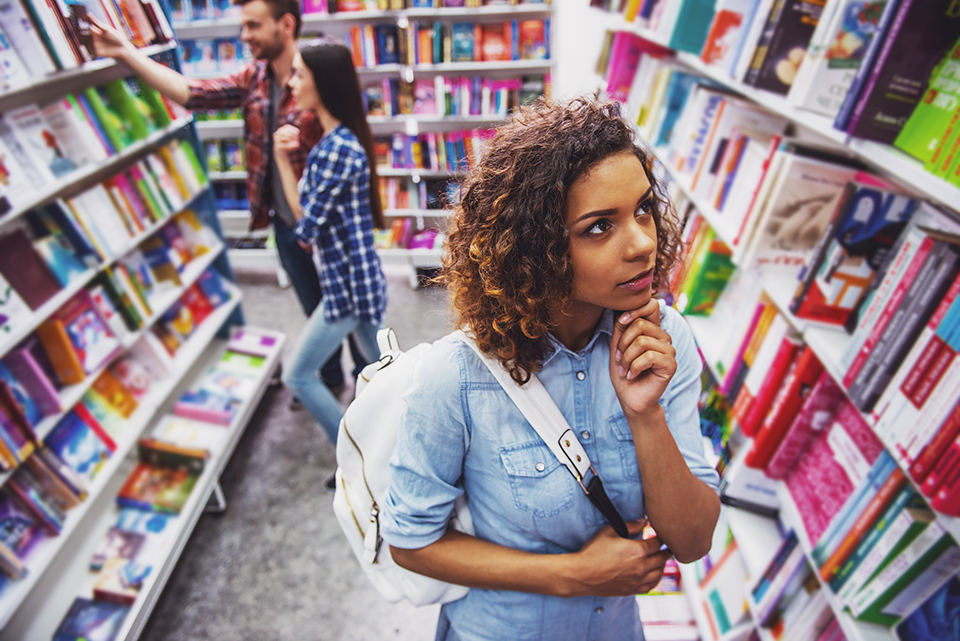 High angle view of a student thinking while choosing book at the bookshop, young man and woman in the background