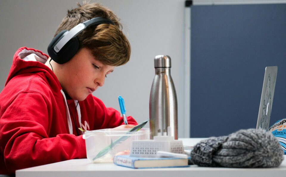 A boy writing something down whilst listening to music on his headphones