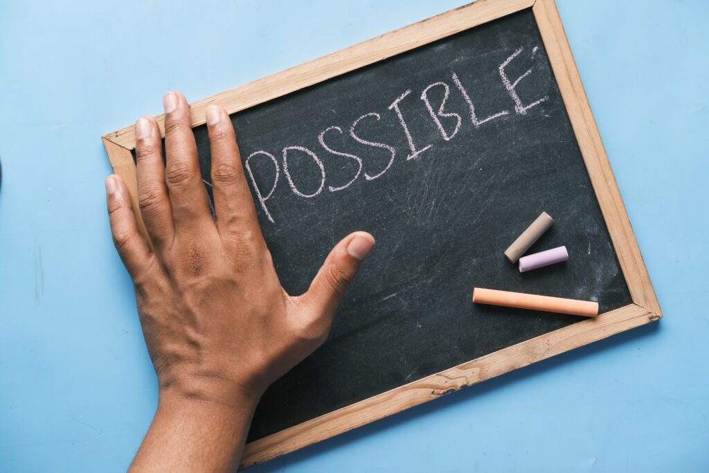 A man covering the letters I and m and leaving the word possible on a chalk board