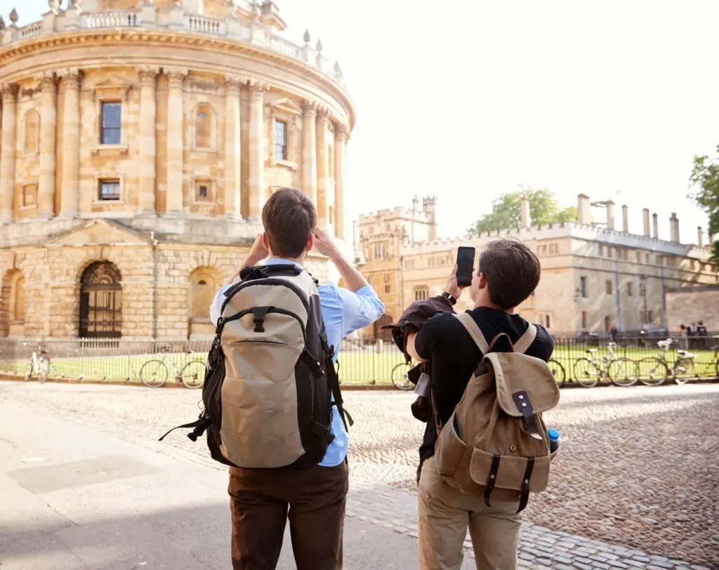 Two Students taking Photos Of Radcliffe Camera Building In Oxford On Mobile Phones