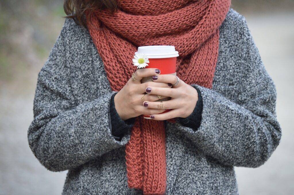 a person wearing a scarf whilst holding a hot drink