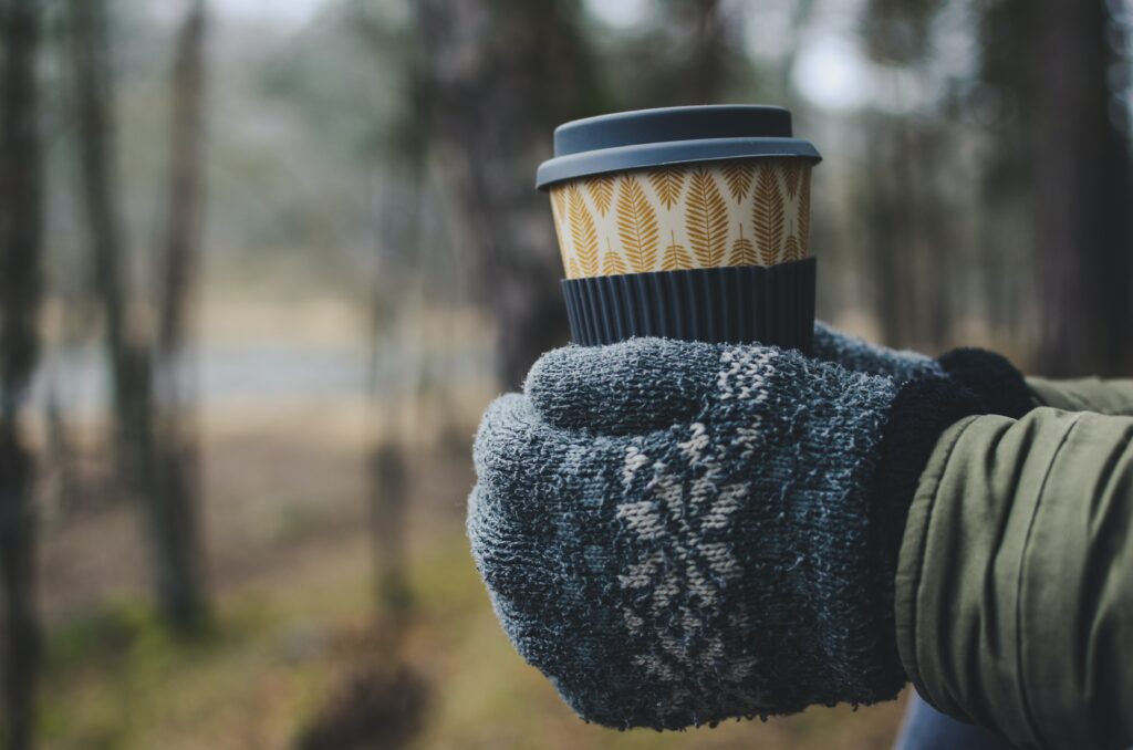 A person wearing gloves holding a hot drink