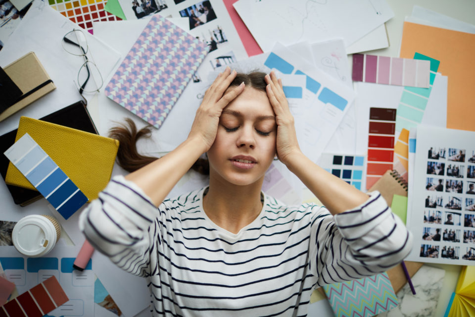 Frustrated Female Student with imposter syndrome lying on the floor surrounded by books, papers and other stationery