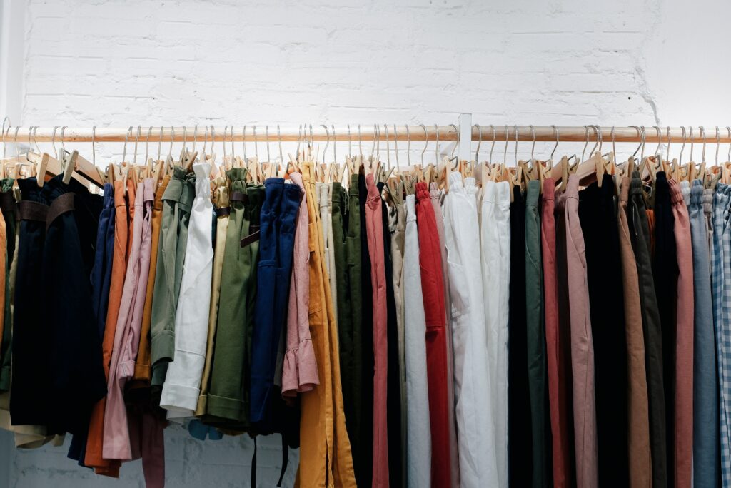 A clothing rack filled with different coloured tops and trousers 