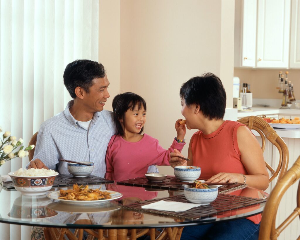 A little girl feeding her mum food whilst on her dad's lap