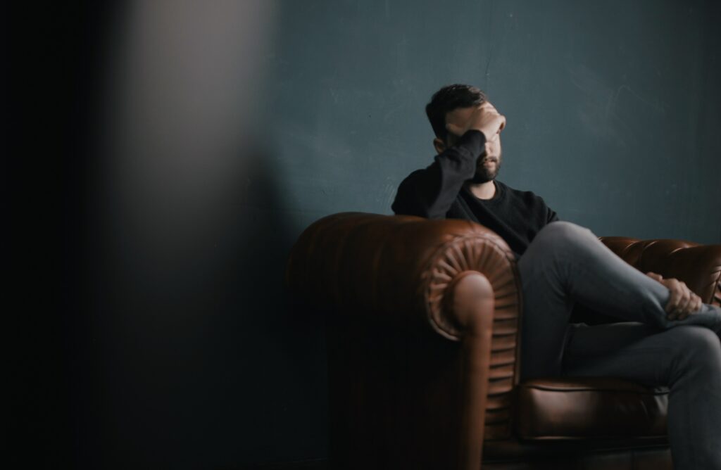 A man putting his hand oh his head sitting on the couch in the dark