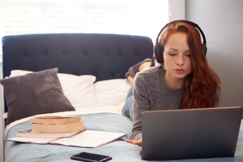 Student wearing headphones on her bed in shared house.