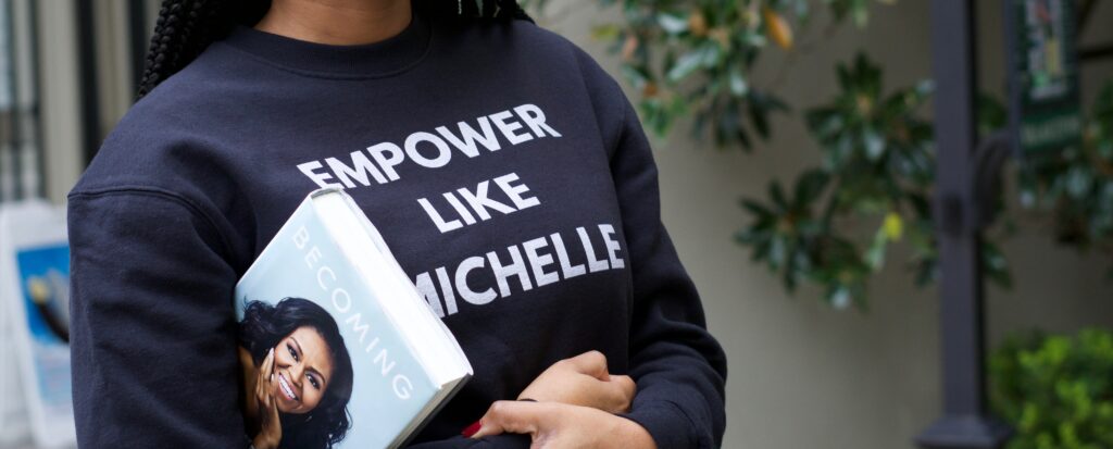 A woman wearing an empower like Michelle jumper whilst holding Michelle Obama's autobiography 