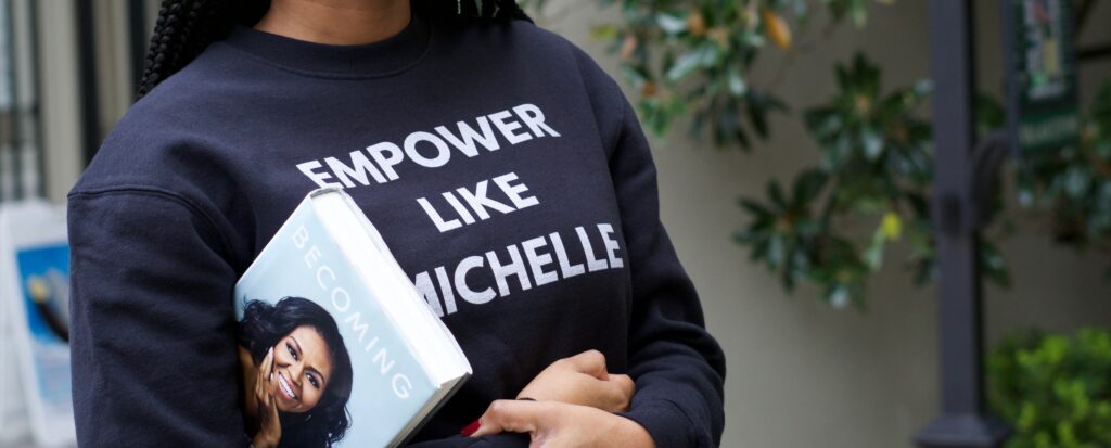 A woman wearing an empower like Michelle jumper whilst holding Michelle Obama's autobiography