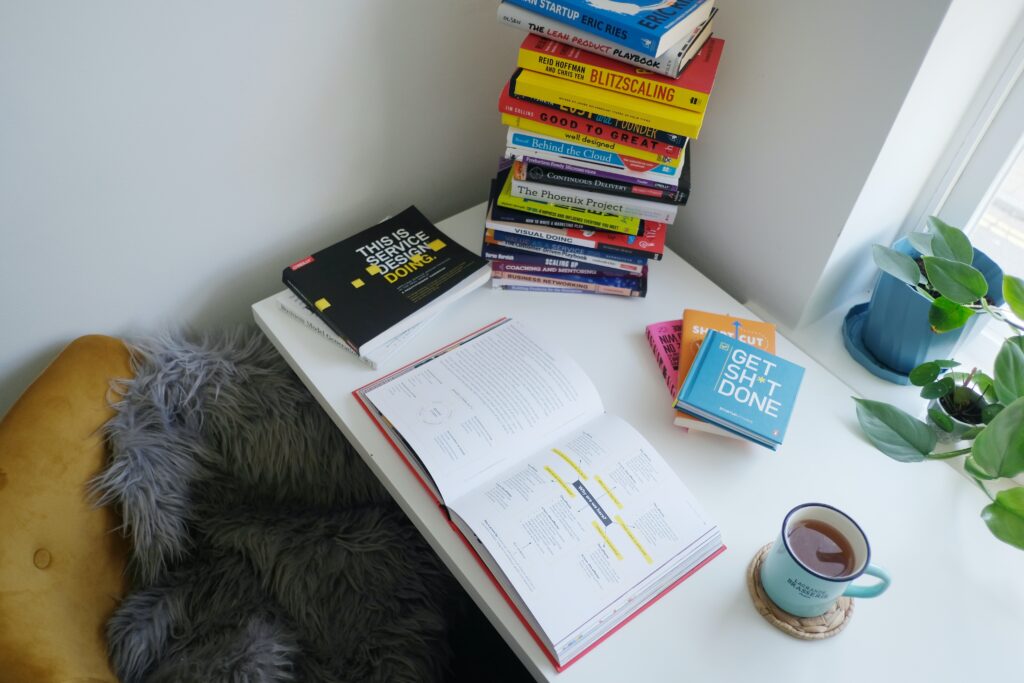 A picture of a stack of books on a desk with a coffee on the side 