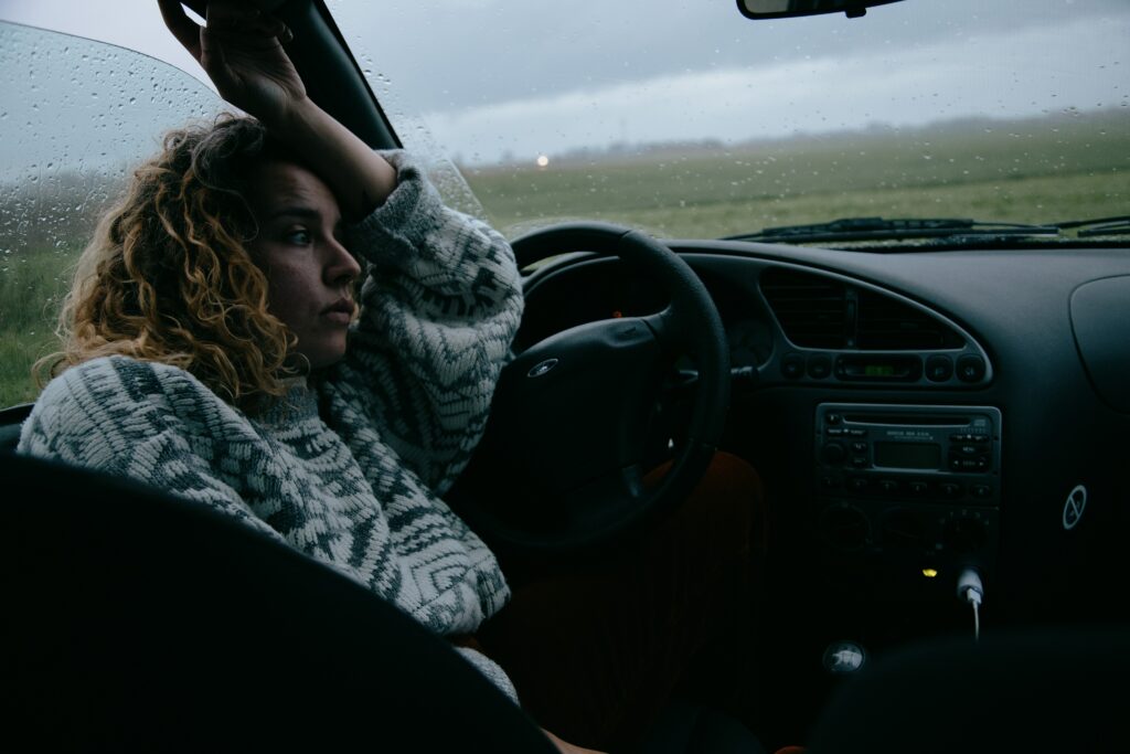 A car sitting in the car whilst its raining looking out the window
