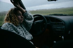 A car sitting in the car whilst its raining looking out the window