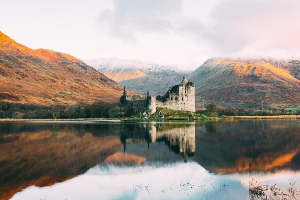 A picture of the Scottish Highlands with a castle in the middle of the water 