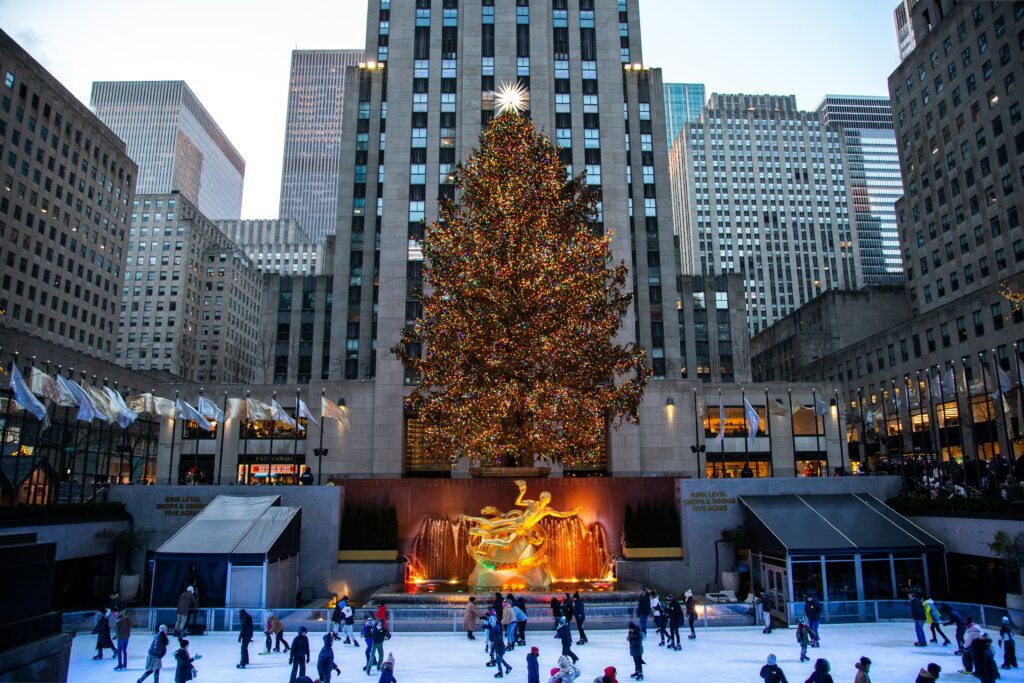 A group of people ice skating in for of a huge Christmas tree 