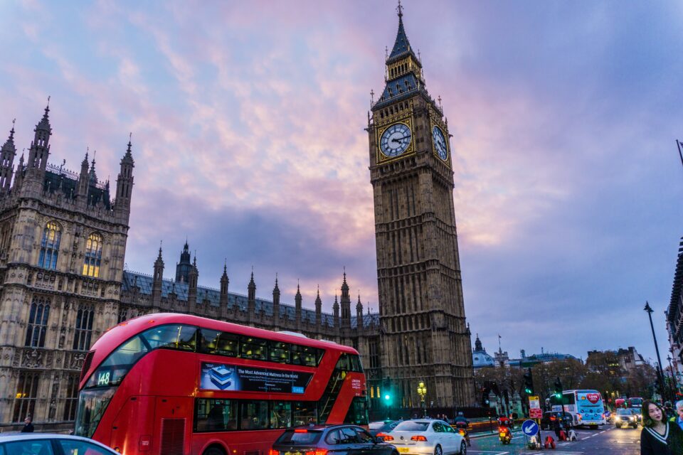 A scenic picture of London with the Big Ben and a red bus passing by