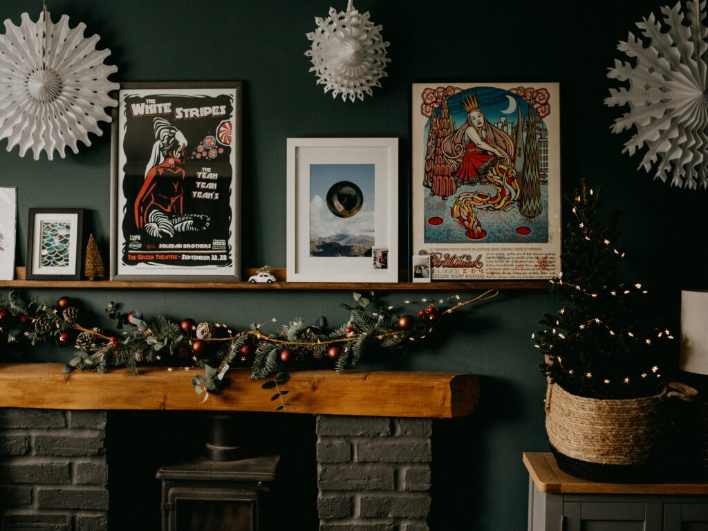 A fireplace with green garland on top of it with some picture frames above it