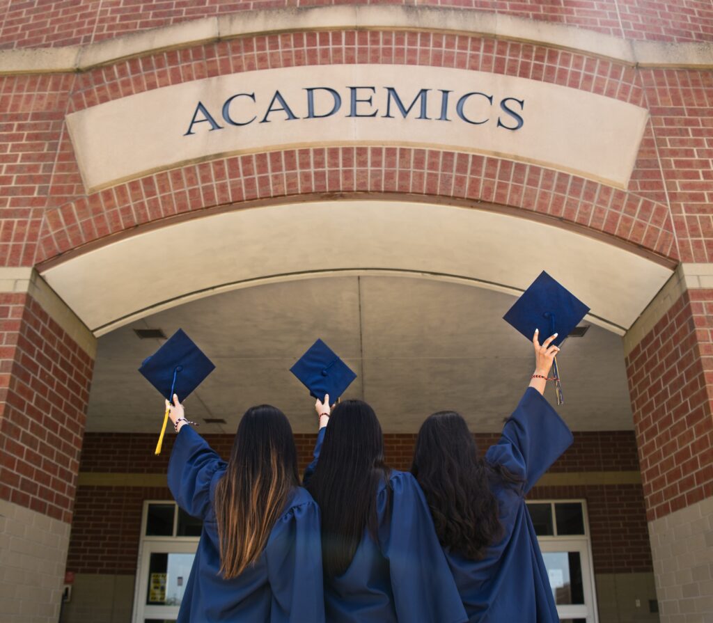 Three girls holding up their graduation hats above their head 