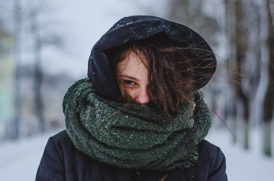 A women facing the camera wrapped up warm with her green scarf in the snow