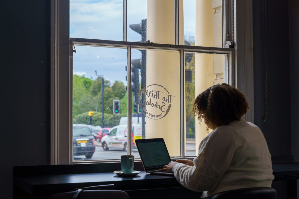 A girl sitting down in a coffee shop with her laptop open