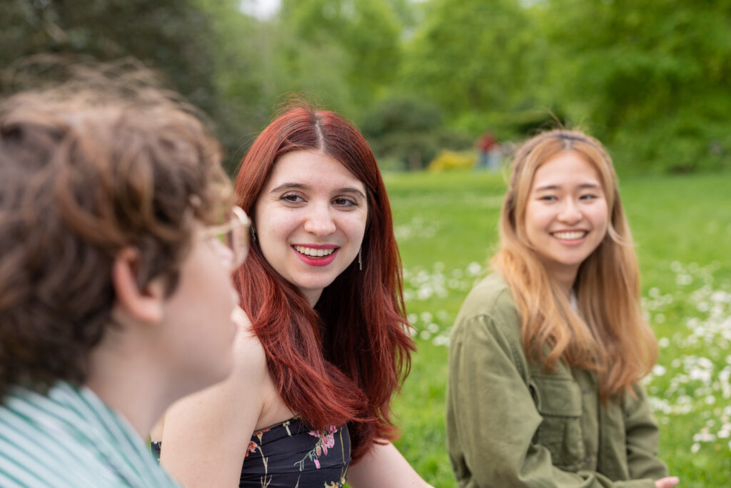 Three women talking whilst sitting on the grass. 