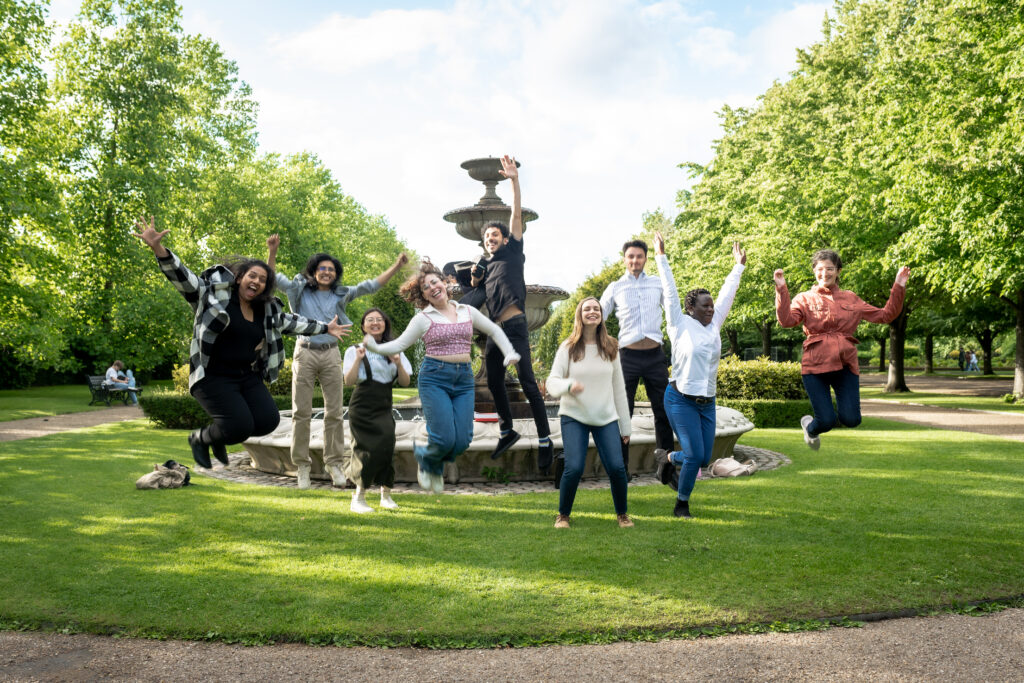 A group of students jumping in front of a fountain 