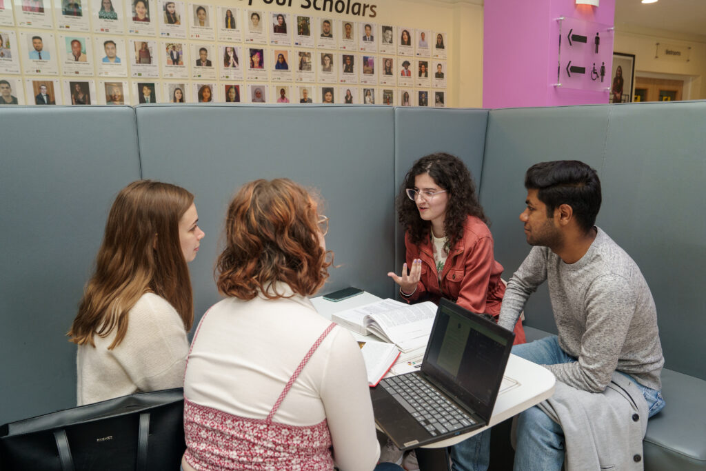 A group of student sitting at a table revising with their laptops and books open. 