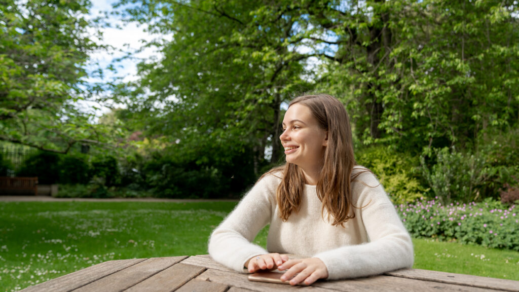 A girl sitting in a park like into the distance.