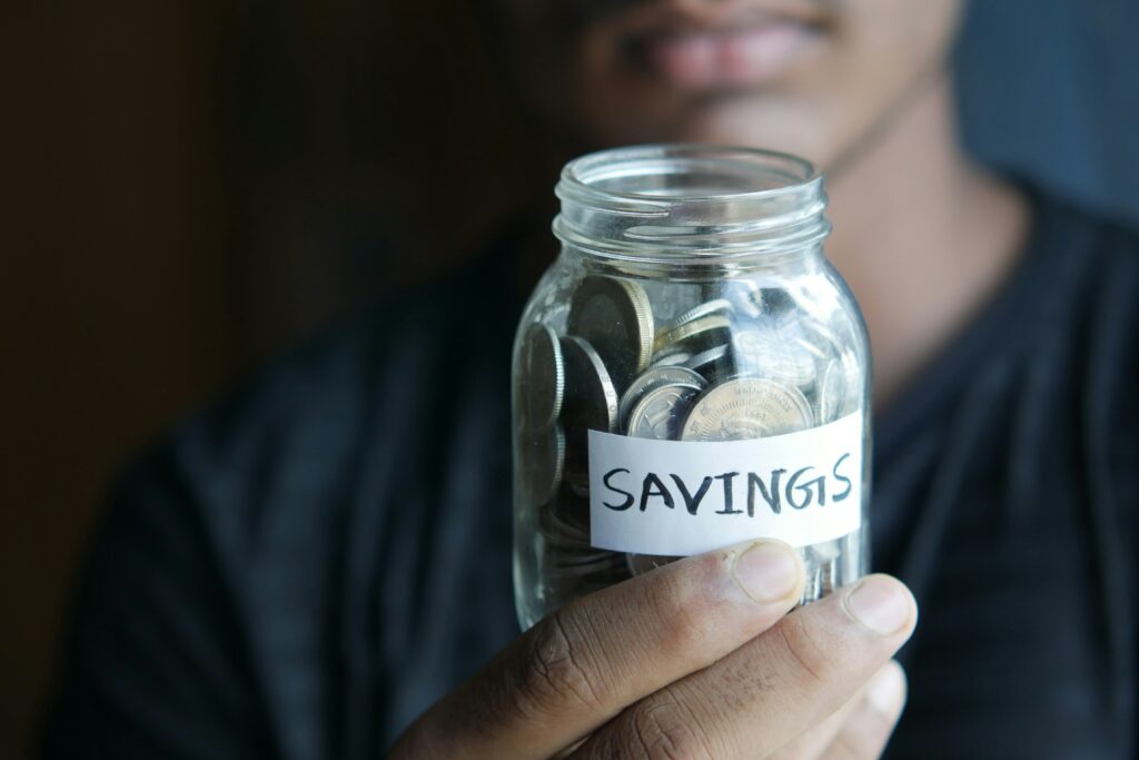 A man holding a jar with coins inside it with words savings outside of it