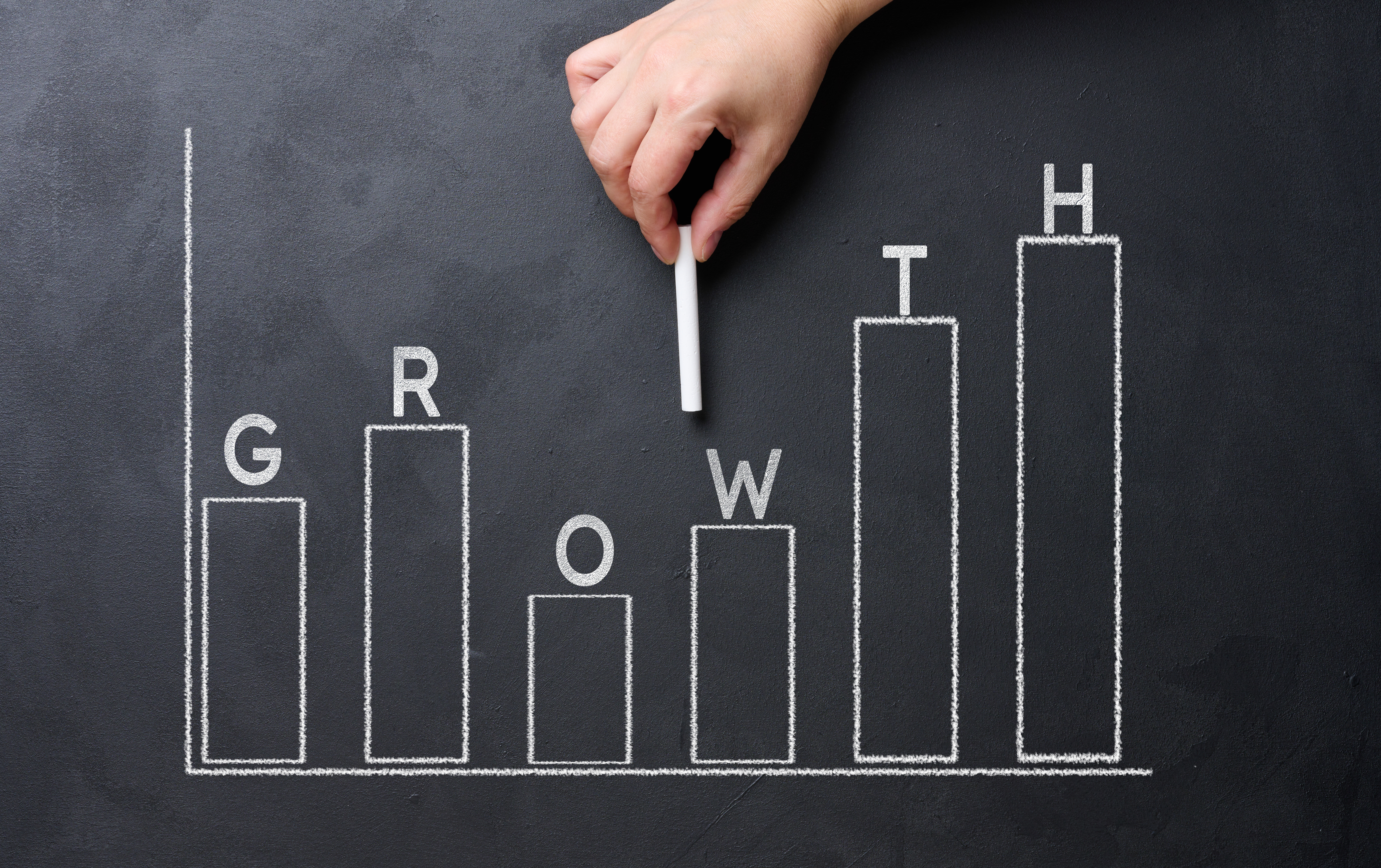 A woman's hand points to a graph with growing indicators drawn on a black chalkboard.