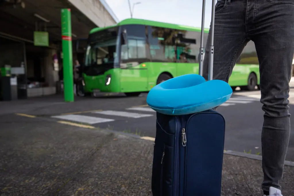 A close up of someone with a suitcase in front of a coach station